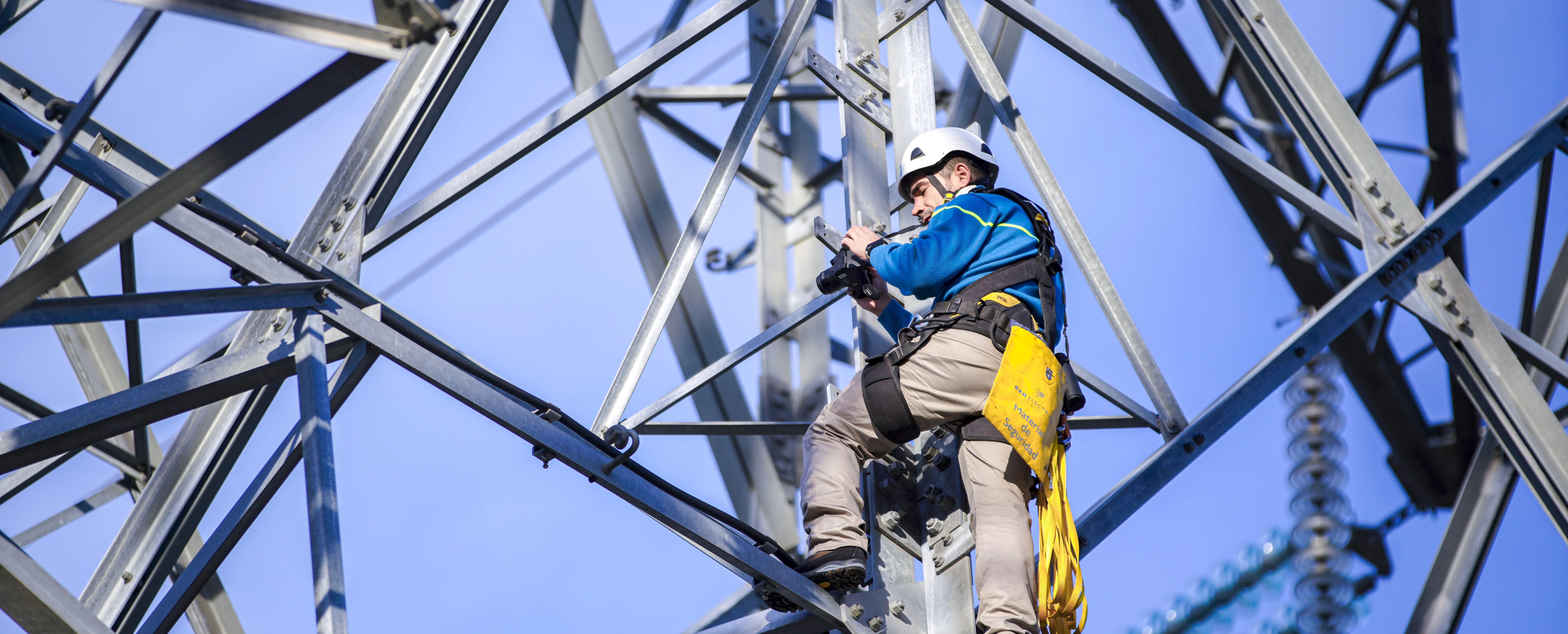Operario con casco y arnés escala una torre eléctrica