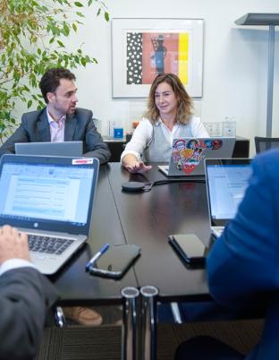 Cuatro personas trabajando en torno a una mesa con sus portátiles e intercambiando opiniones