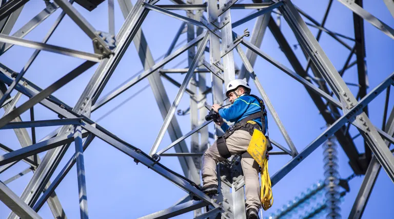 Operario con casco y arnés escala una torre eléctrica