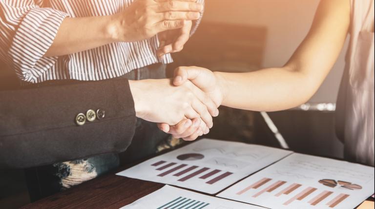 Hands shaking hands over documents with charts