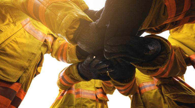 Cinco bomberos formando un círculo juntando sus manos en el centro