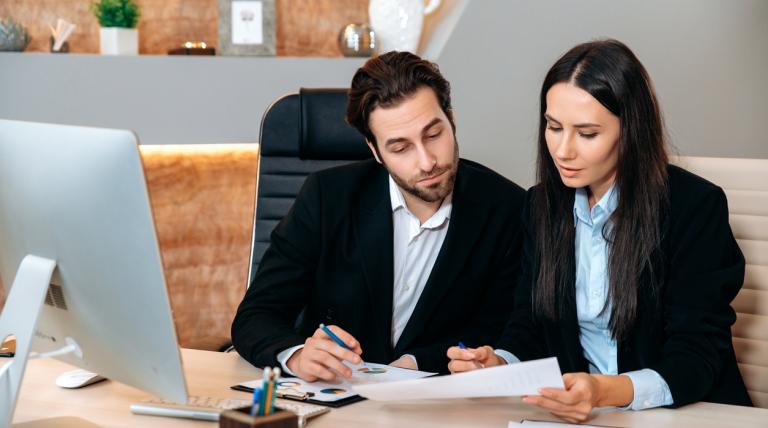 Dos compañeros de trabajo consultando unos datos de un papel en su mesa de trabajo