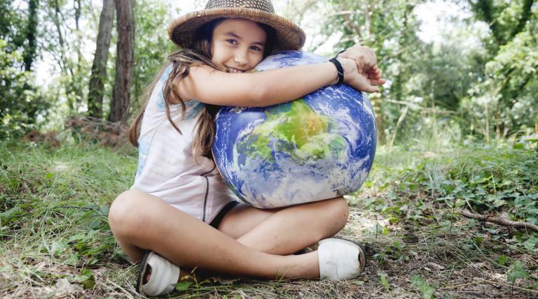 Niña sentada en un bosque abrazando una bola del mundo