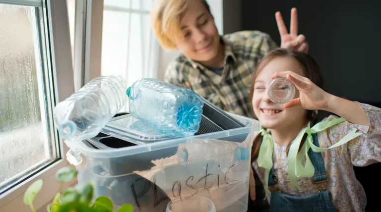 Dos niños sonriendo con una cajacon envases de plástico para reciclar