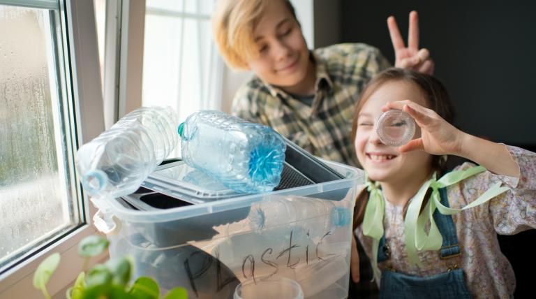 Dos niños sonriendo con una cajacon envases de plástico para reciclar