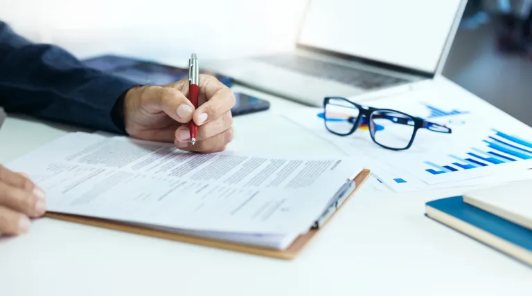 Persona escribiendo sobre una hoja en una mesa llena de documentos