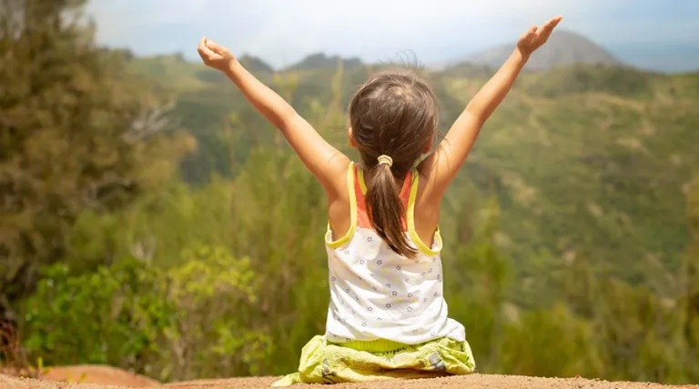 Niña de espaldas con los brazos extendido mirando el horizonte