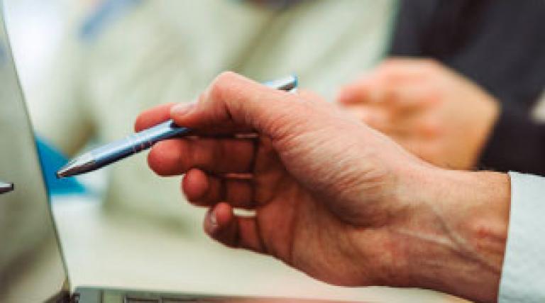 Person pointing to the screen of a laptop with a ballpoint pen