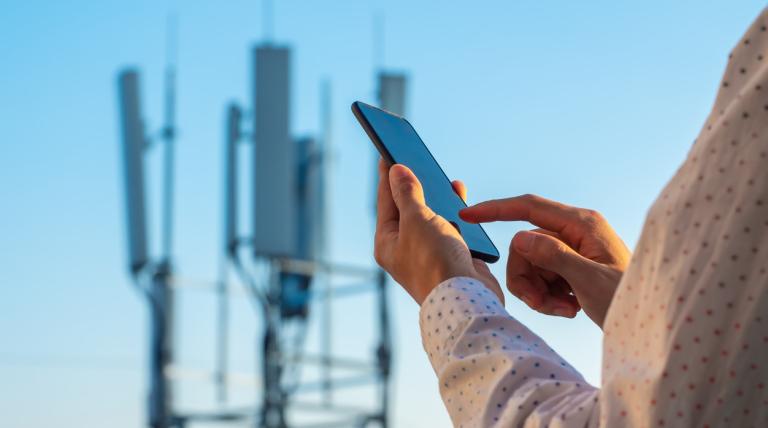 Foto de una persona utilizando un móvil con una antena telefónica de fondo